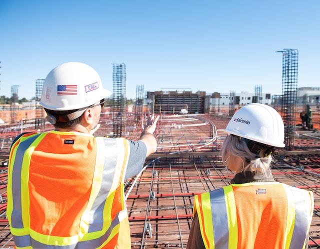 photo of the backs of two workers in construction outfits looking onto a construction site